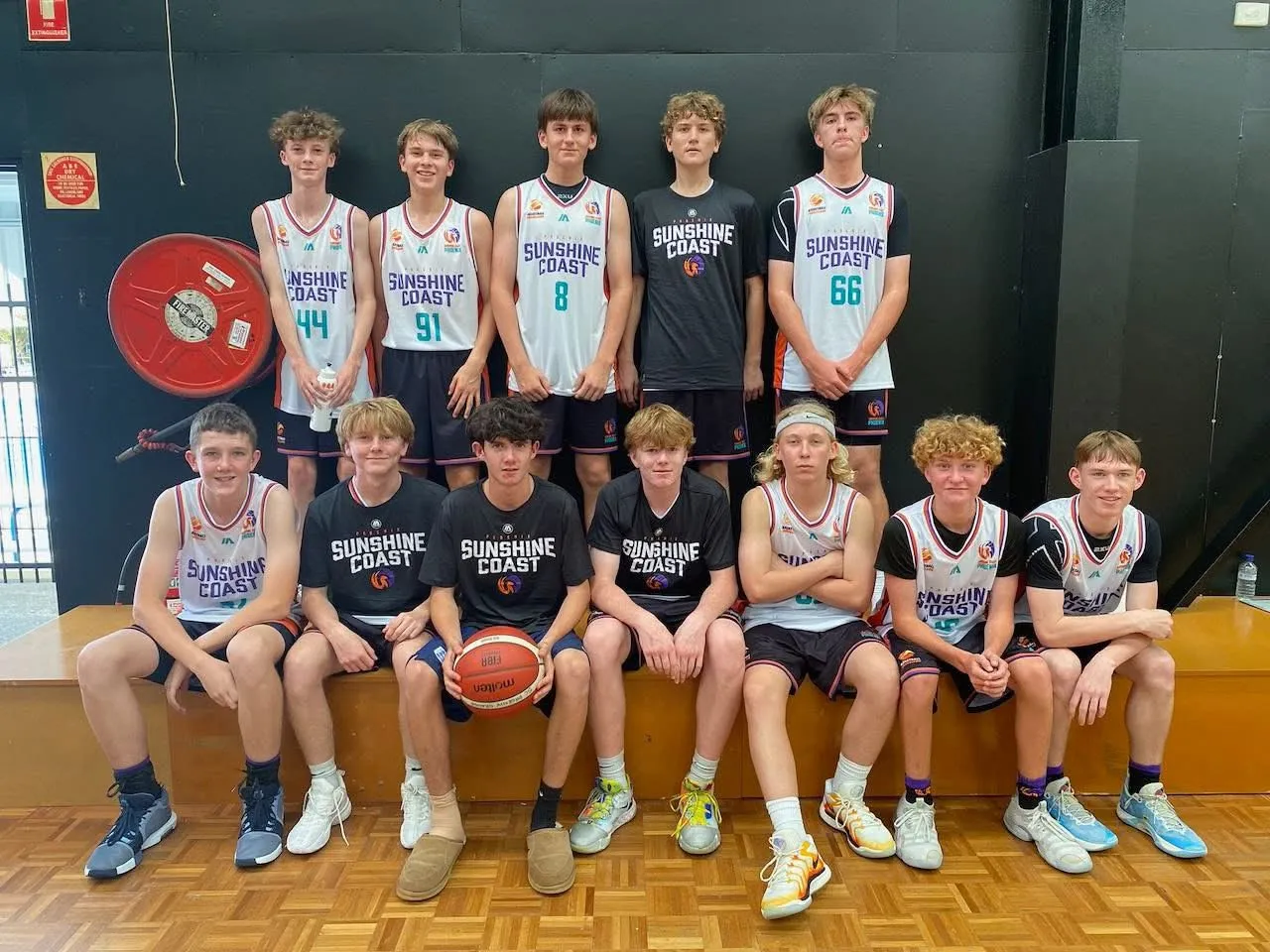 The Under 16 Sunshine Coast Phoenix basketball squad in team singlets, posed in two rows in the stadium
